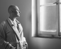 Bald woman suffering from cancer looking throught the hospital window.