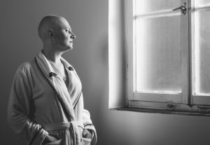 Bald woman suffering from cancer looking throught the hospital window.